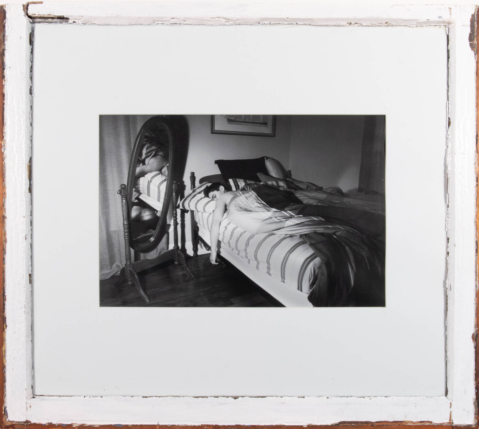 Black and white photograph of a person sleeping in a bed with a mirror next to them, reflecting the scene.